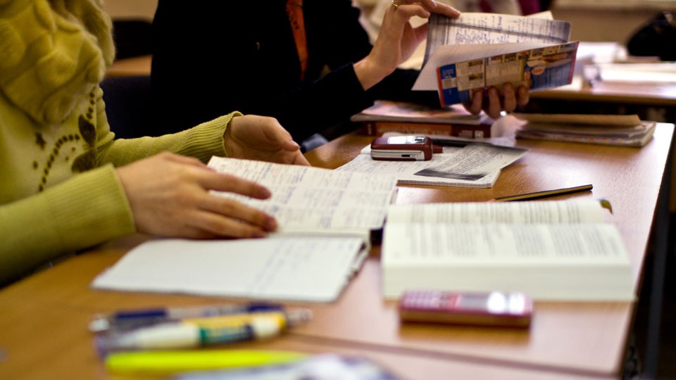 Personer studerar i ett klassrum. Läser i böcker och skriver i block. Foto. 