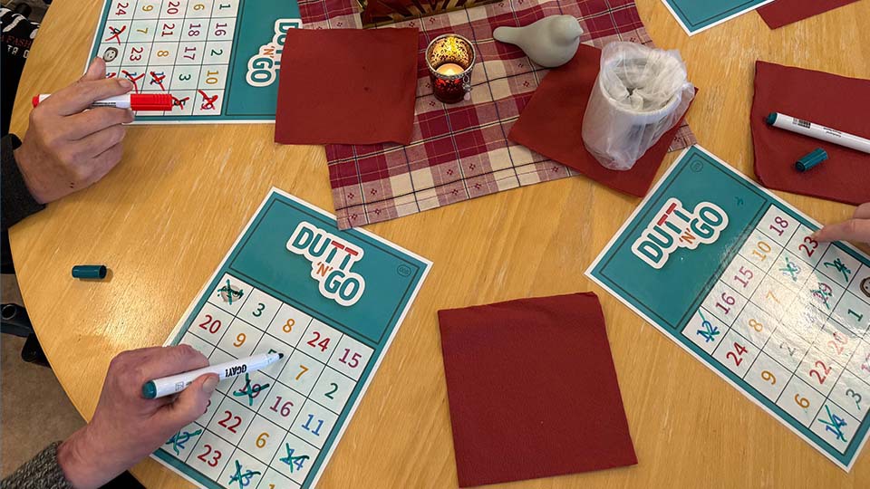 Händer som spelar bingo med pennor och brickor på ett bord.