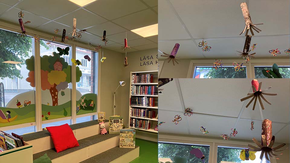 Kollage av bilder på fjärilar och rymdraketer skapade av barn, upphängda i taket i ett bibliotek.