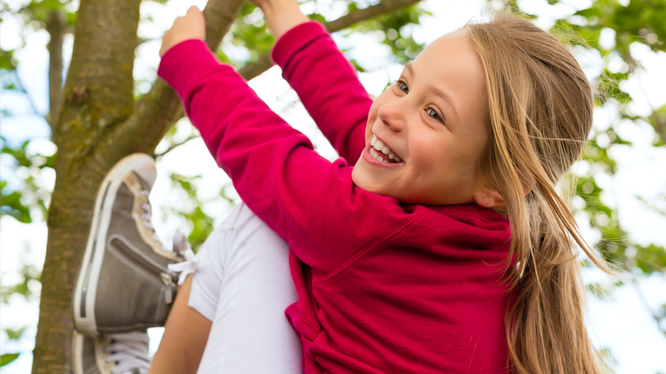 En flicka som skrattar och klättrar i ett träd. 