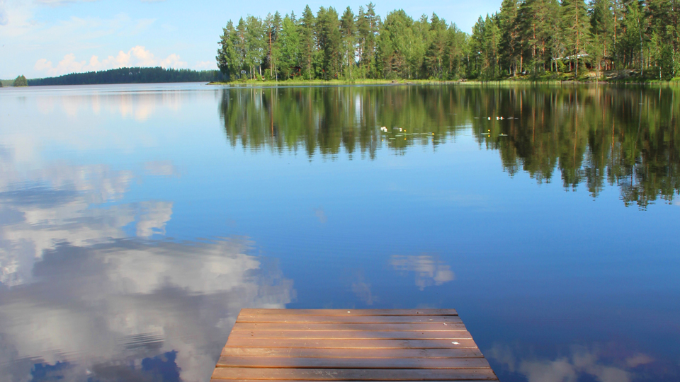 En sjö med en brygga i och skog i slutkanten av sjön.