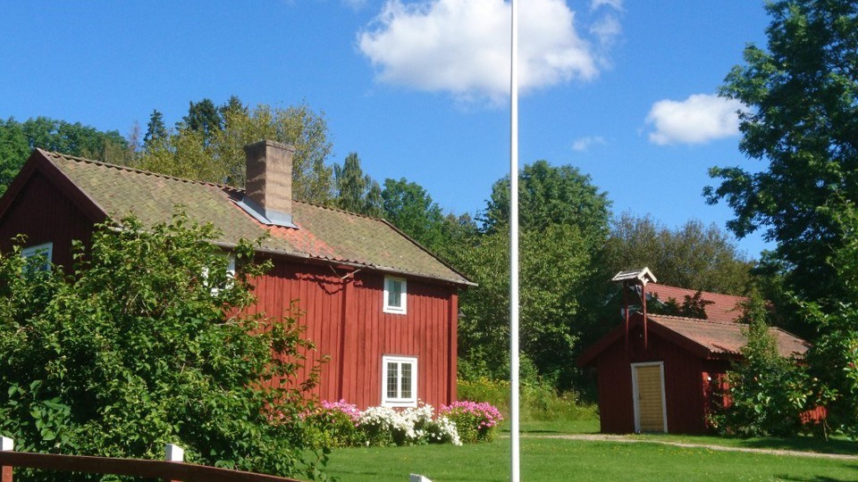Röd stuga med vita knutar i grönt landskap