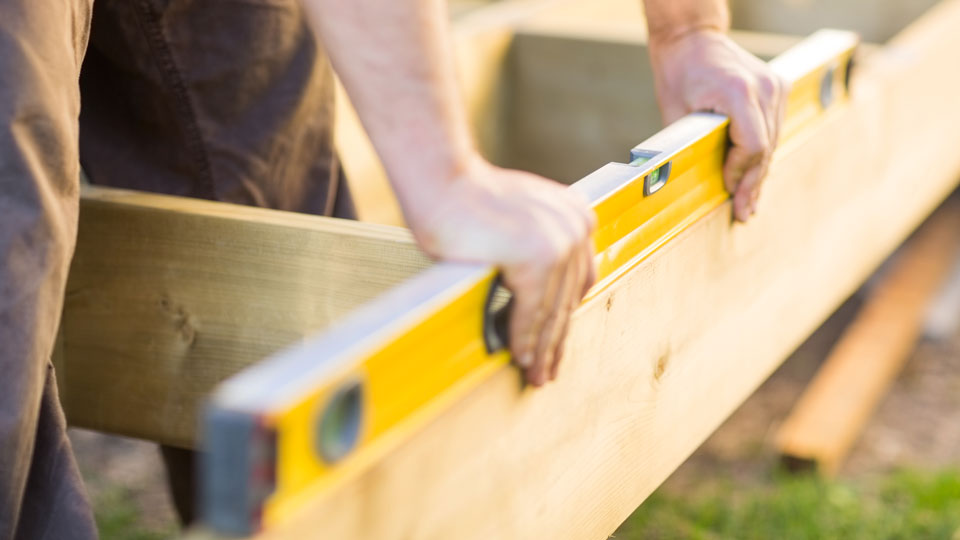 Person mäter med vattenpass på en bräda i trä. Foto.