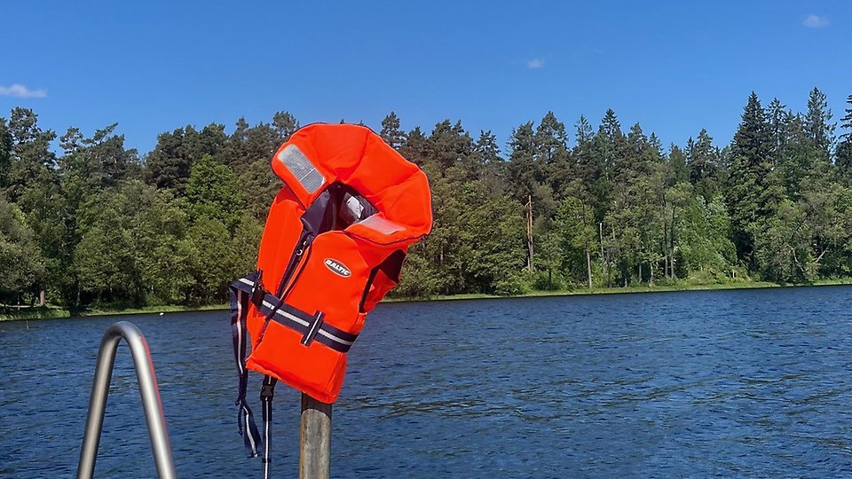 Flytväst som hänger på en stolpe vid en sjö. Foto