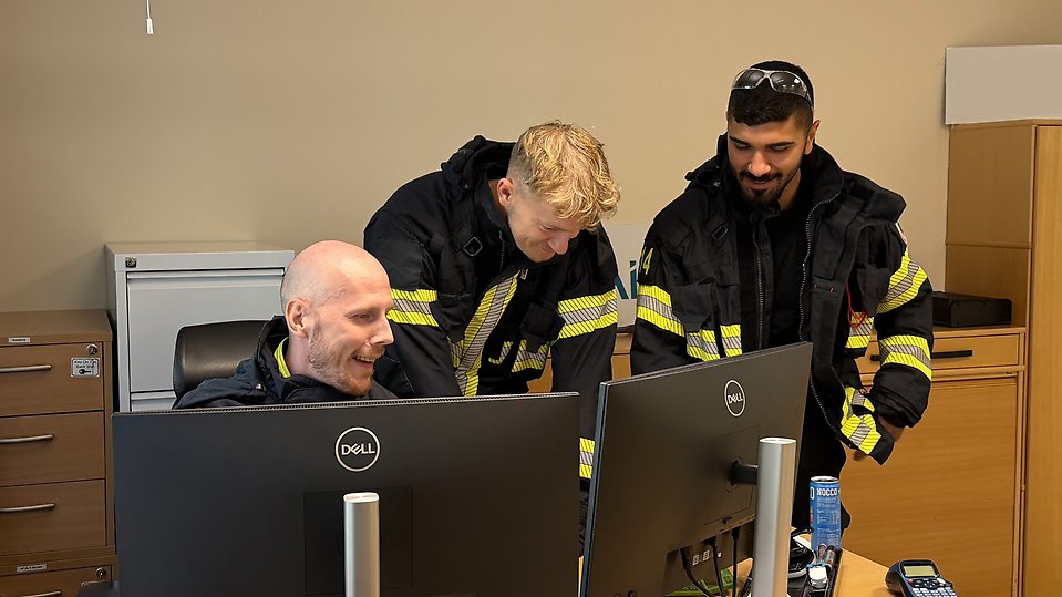 Rasmus, Hugo och Modi står vid en dator på ett kontor och planerar dagens arbetsuppgifter. Foto.