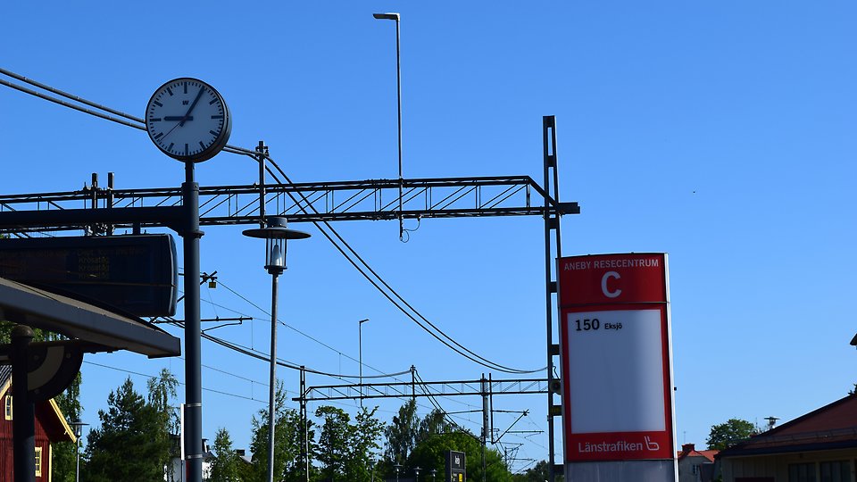 Klocka, hållplats och ledningar för tåg. Foto. 