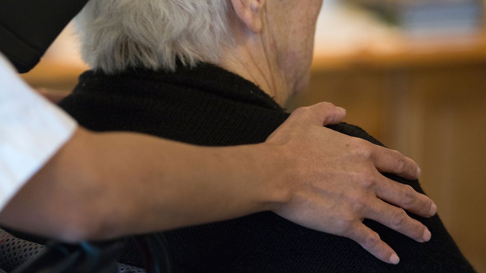 En person håller sin hand på en äldre persons axel. Foto.