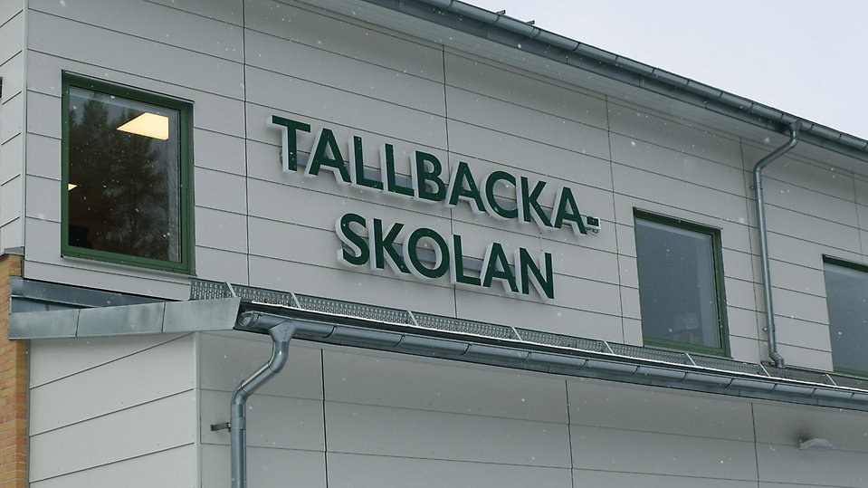 Bild på Tallbackaskolans fasad med en skylt där det står Tallbackaksolan 