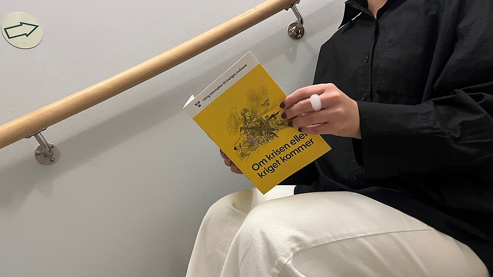 Person som sitter i en trappa och läser "Om kriget eller krisen kommer". Foto 
