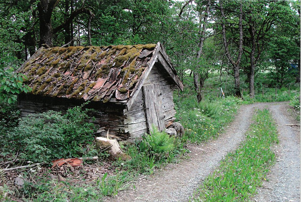 Foto föreställande lada och väg, med stengärde bredvid. 